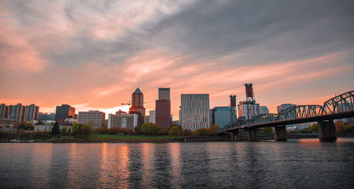 Scenic view of river by buildings against sky during sunset