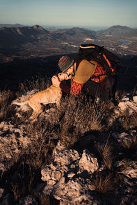 Full length of man with dog on rock against sky