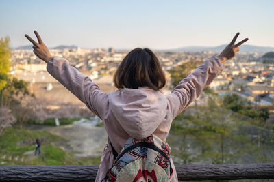 Rear view of woman with arms raised standing against sky