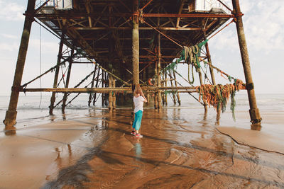 Full length of woman standing below pier on shore at beach