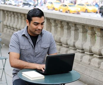 Smiling young man using laptop at sidewalk cafe