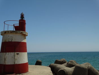 Lighthouse by sea against clear blue sky