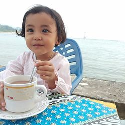 Portrait of cute girl sitting on table by sea