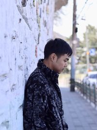 Boy looking away while standing against wall