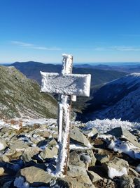Cross on snow covered mountains against blue sky