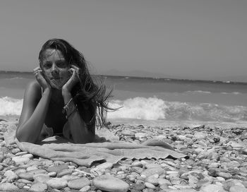 Young woman with pebbles on beach against sky