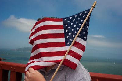 Person face covered with amercian flag against sea