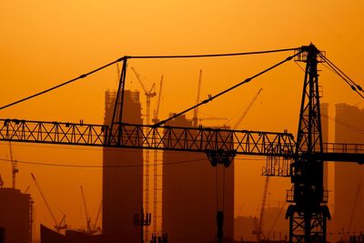 Silhouette cranes at construction site against sky during sunset