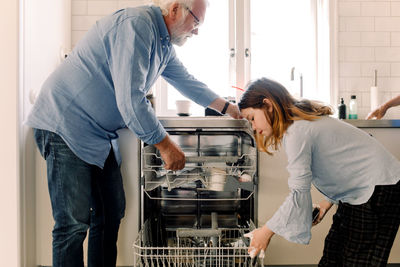 Grandfather assisting granddaughter in cleaning dishwasher at kitchen