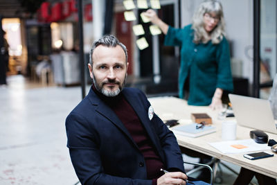 Portrait of smiling businessman sitting by table in meeting at office