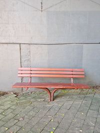 Empty bench on footpath against wall