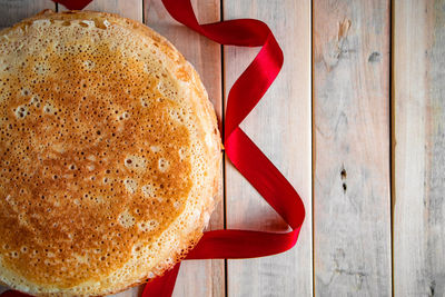 Traditional russian thin pancakes closeup on a light wooden background and a red ribbon.