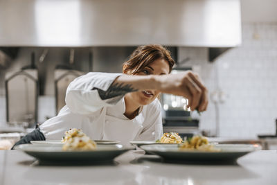 Female chef sprinkling cheese on tagliatelle pasta at kitchen counter in restaurant