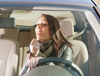 Young woman applying lipstick while sitting in car