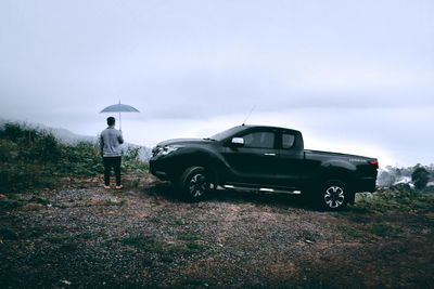 Man standing by car on road during rainy season