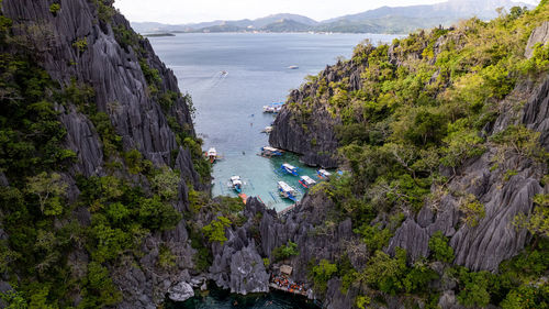 In the photo, a vibrant tropical boat near a beautiful beach or rocky shore.