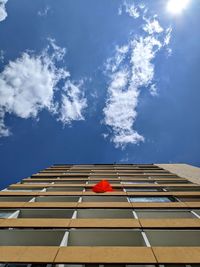 Low angle view of red umbrella on the buildings' middle floor against sunny blue sky