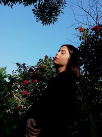 Low angle view of young woman standing against trees