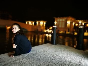 Portrait of woman sitting on retaining wall against sky at night