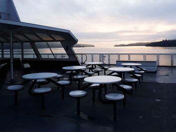 Chairs and table by sea against sky during sunset