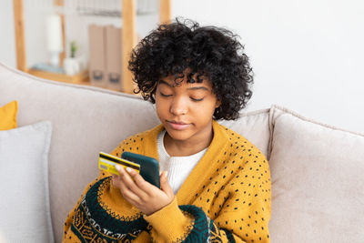 Young woman using phone while sitting on sofa at home