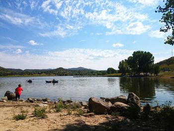 Man sitting by lake against sky