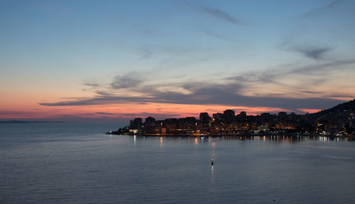 Scenic view of sea by buildings against sky at sunset