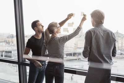 Business people discussing over adhesive notes stuck to glass window