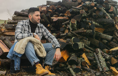 Young man sitting on firewood in forest