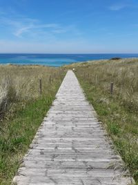 Footpath leading towards sea against sky