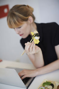 Businesswoman having sushi while using laptop at table in office