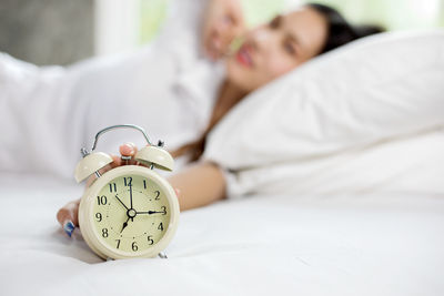 Woman holding alarm clock while lying on bed at home