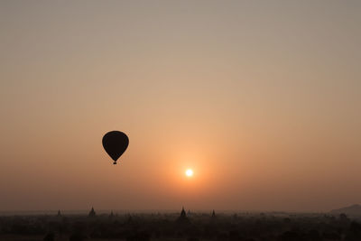 Hot air balloon flying over historic temples against sky during sunset