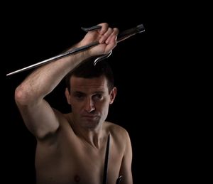 Portrait of shirtless man holding weapon against black background