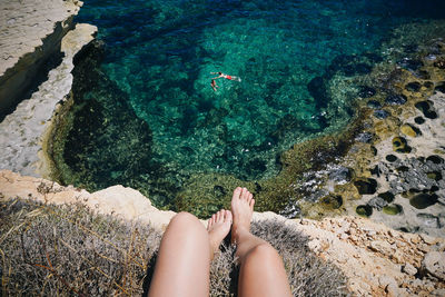 Low section of woman sitting on cliff against sea