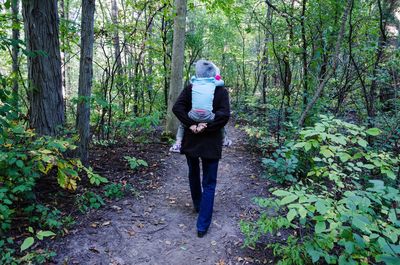 Rear view of grandmother piggybacking granddaughter on footpath amidst trees