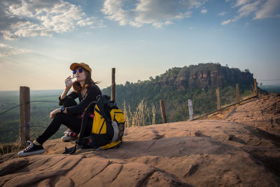 Full length of man sitting on mountain against sky