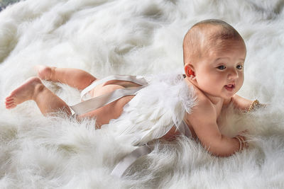 High angle view of cute baby girl lying over fur blanket on bed at home