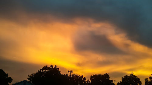 Silhouette trees against dramatic sky during sunset