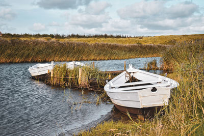 Boat moored on field by lake against sky