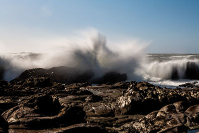 Long exposure of waves crashing over coastal rocks under blue sky