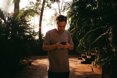 Man using smart phone while standing against tree