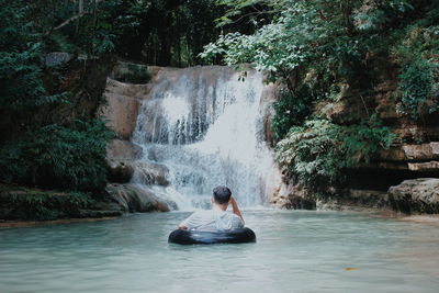 Man sitting on rock against waterfall