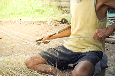 Midsection of man cutting wood while sitting on field