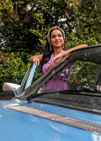 Smiling young woman standing by car