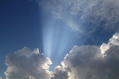 Low angle view of sunlight streaming through clouds