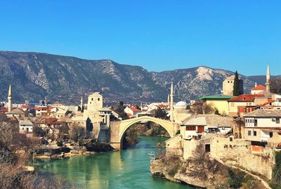 Bridge over river amidst buildings in town against clear blue sky