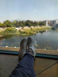 Low section of person relaxing on glass against sky