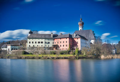 Buildings by lake against blue sky