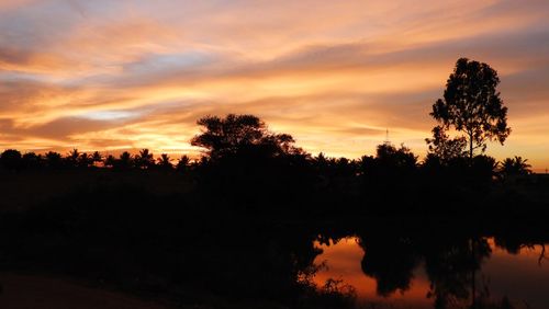 Silhouette trees by lake against romantic sky at sunset